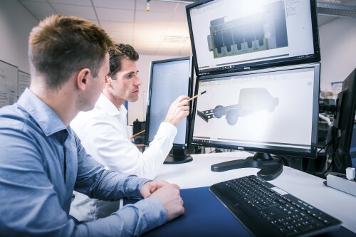 Two men sit at a computer with three screens