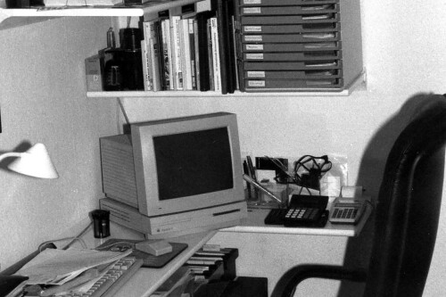 Black and white image of an office with computer and telephone.